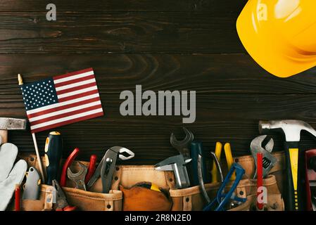 Attrezzi hardHat toolbelt e noi bandiera su sfondo di legno banner del giorno di lavoro mockup Foto Stock