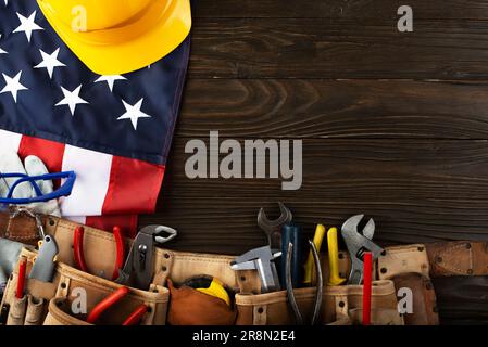 Attrezzi hardHat toolbelt e noi bandiera su sfondo di legno banner del giorno di lavoro mockup Foto Stock