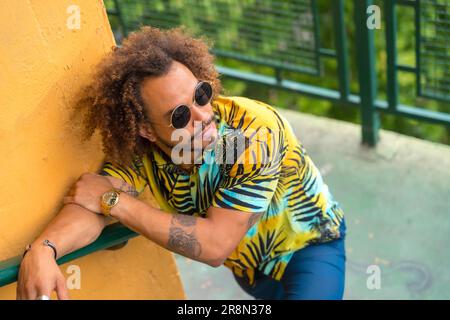 Passato di un uomo attraente con capelli afro in una camicia estiva di palma su uno sfondo giallo e una scala Foto Stock