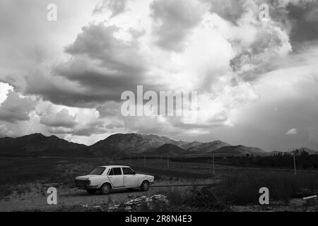 Un'immagine in scala di grigi di una vecchia auto abbanonata parcheggiata in un vasto paesaggio desertico Foto Stock