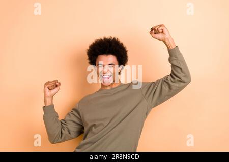 Ritratto di giovane uomo overjoyed indossare elegante bruno jumper sollevare pugni in su grida celebrare vittoria shopping giorno isolato su sfondo di colore beige Foto Stock