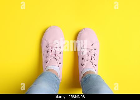 Donna in sneaker eleganti in piedi su sfondo giallo, vista dall'alto Foto Stock