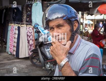 Un tassista del motociclo (xe om) fuma una sigaretta mentre attende i passeggeri fuori dal mercato centrale di Kontum, nelle Highlands centrali di Vietn Foto Stock