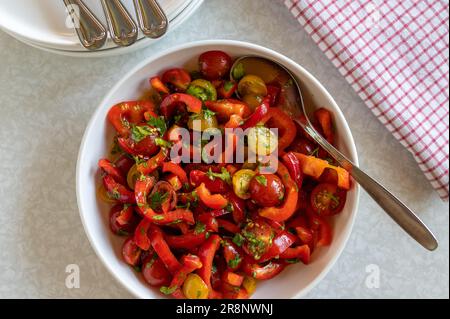 Insalata con peperoni, pomodori ciliegini rossi e gialli in un recipiente con cucchiaio Foto Stock