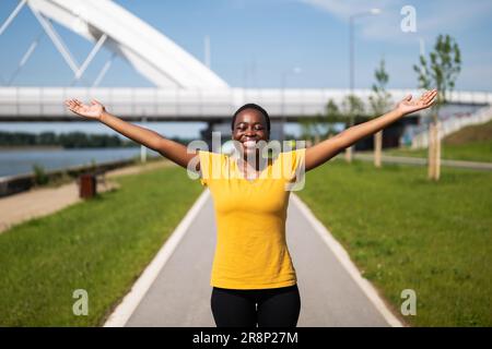 Una donna sportiva si diverte in una giornata di sole con le braccia allungate all'aperto. Foto Stock