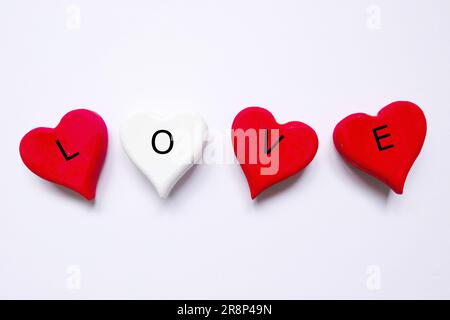 Vista dall'alto del simbolo bianco e rosso del cuore artigianale in legno scritto con "AMORE" su sfondo bianco. Tema di San Valentino. Foto Stock