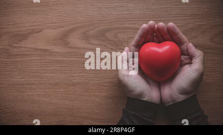 Una mano che tiene il cuore o l'oggetto a forma d'amore su sfondo di legno con spazio per la copia. Foto Stock