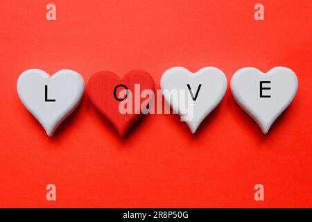 Vista dall'alto del simbolo bianco e rosso del cuore artigianale in legno scritto con "AMORE" su sfondo rosso. Tema di San Valentino. Foto Stock