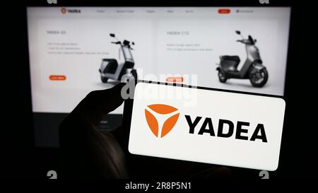 Persona che possiede il cellulare con il logo della società cinese Yadea Group Holdings Ltd. Sullo schermo davanti alla pagina Web aziendale. Concentrarsi sul display del telefono. Foto Stock