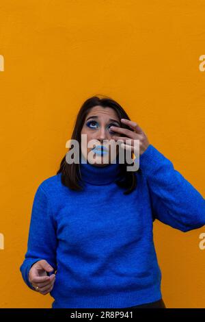 Una giovane donna caucasica che indossa una camicia blu con un'espressione sorpresa sul viso, guardando verso la macchina fotografica con una mano fino alla guancia Foto Stock