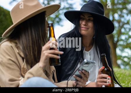Due amici sorridono e gustano una birra insieme all'aperto in un parco Foto Stock