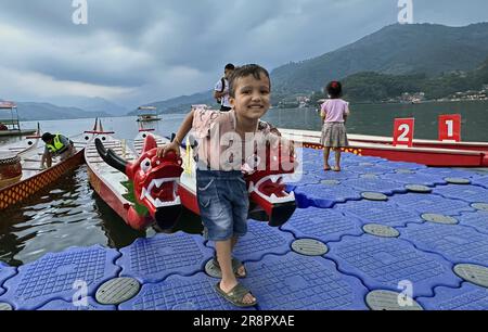 22 giugno 2023, Pokhara, Gandaki, Nepal: Un bambino nepalese gesta con barche a forma di drago che si preparano per il ''Nepal-Cina Friendship Dragon Boat Race Festival'' presso il lago Phewa a Pokhara, Nepal il 22 giugno 2023. Nepal-Cina Friendship Dragon Boat Race Festival si terrà a Pokhara il 23 e 24 giugno, segnando la prima volta che un tale evento si terrà in Asia meridionale. Il festival è organizzato congiuntamente dal Nepal Tourism Board, Ambasciata cinese in Nepal, e Pokhara Metropolitan City, con il Pokhara Tourism Council (PTC) e Nepal-China Overseas Association in qualità di co-organizzatori. A. Foto Stock