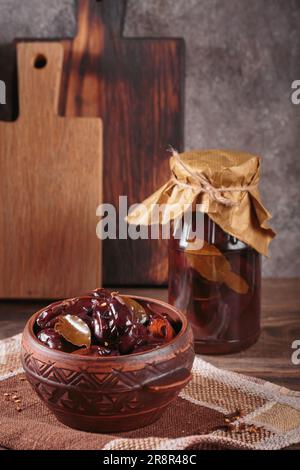 Prugne marinate con spezie in vaso di vetro sul tavolo da cucina Foto Stock