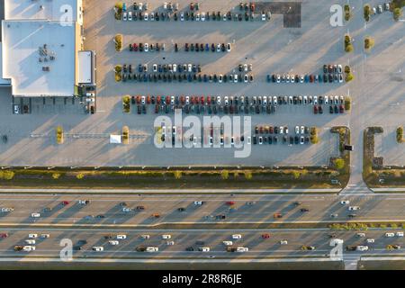 Ampio parcheggio del concessionario locale con molte auto nuove parcheggiate in vendita sul lato dell'autostrada. Sviluppo dell'industria automobilistica americana e. Foto Stock