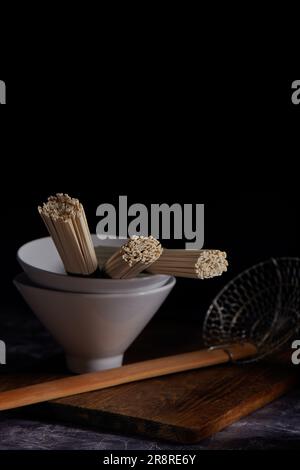 Tagliatelle udon di grano crudo in ciotola in ceramica di stile asiatico, cucina orientale e asiatica, chiave scura Foto Stock