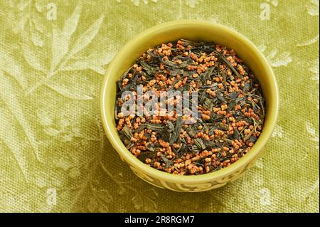 Genmaicha giapponese, tè verde con riso arrosto, una ciotola su sfondo tessile verde con uno spazio copia Foto Stock