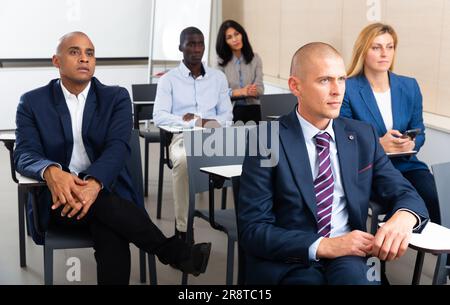 Gruppo internazionale di uomini d'affari che ascoltano la presentazione ai tavoli Foto Stock