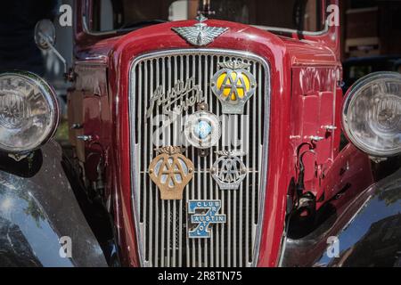 Vista frontale dettagliata di una Austin Seven rossa degli anni '1930 con vari stemmi automobilistici sulla griglia del radiatore. Austin Ruby ad una mostra d'auto d'epoca. Foto Stock