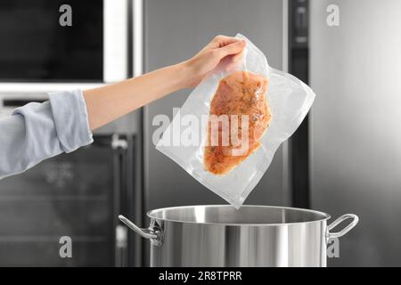 Donna che mette carne confezionata sottovuoto in pentola in cucina, primo piano Foto Stock