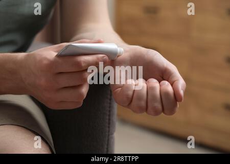 Uomo che applica unguento dal tubo al polso in casa, primo piano Foto Stock