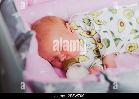 Un neonato beve autonomamente latte o una miscela secca da un biberon, a casa Foto Stock