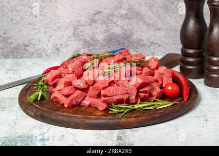 Carne cruda di manzo tagliata a cubetti. Manzo o agnello a dadini su una tavola di legno Foto Stock