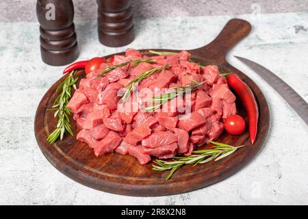 Carne cruda di manzo tagliata a cubetti. Manzo o agnello a dadini su una tavola di legno Foto Stock