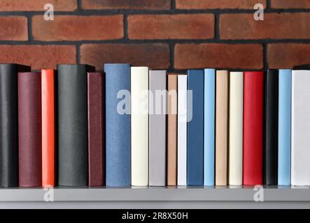 Molti libri con copertina rigida diversi su un tavolo grigio vicino al muro di mattoni Foto Stock