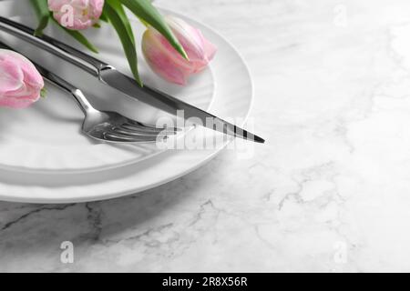 Elegante ambiente da tavolo con posate e tulipani su sfondo di marmo bianco, primo piano. Spazio per il testo Foto Stock