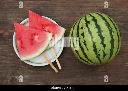 Cocomeri maturi interi e affettati su tavola di legno, piatto Foto Stock