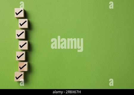 Cubi in legno con segni di spunta su sfondo verde, a terra. Spazio per il testo Foto Stock