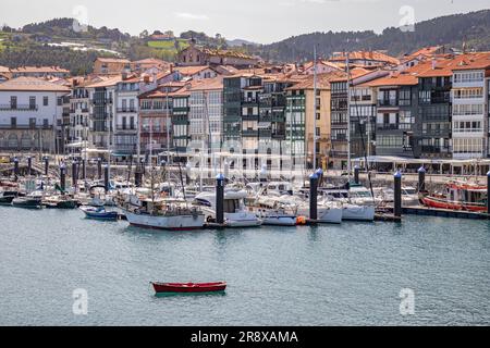 Lekeitio, Spagna - 30 marzo 2023: Vista del porto con barche ancorate, case alte e strette, colline e foreste sullo sfondo Foto Stock