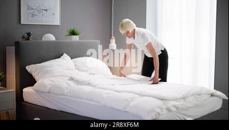 Young Female Housekeeper Changing Bedding In Hotel Room Foto Stock