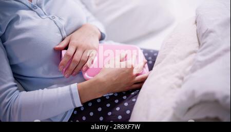 Young Woman With Hot Water Bottle On Stomach Lying In Bed Stock Photo