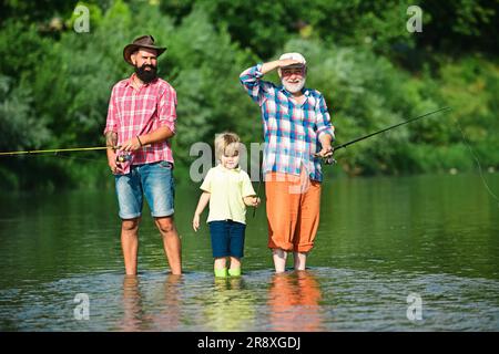 Hobby e attività sportive. Un uomo che insegna ai bambini a pescare nel fiume. Felice nonno, padre e nipote con canne da pesca sull'ormeggio sul fiume Foto Stock