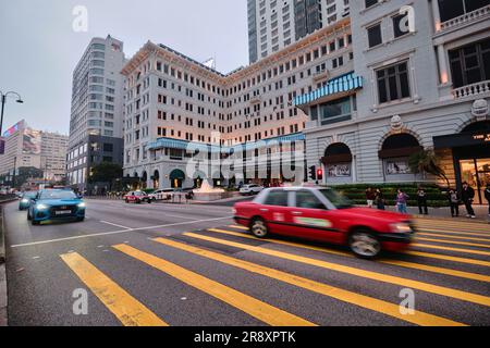 Hong Kong, Cina - 24 aprile 2023: Hotel The Peninsula e taxi rosso sulle strisce gialle di attraversamento Foto Stock