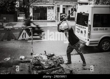 Un operaio frantuma il cemento con una mazza sul marciapiede di Danang, in Vietnam. Foto Stock