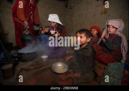 I bambini Wakhi e la loro madre mangiano zuppa in una capanna di fango al campo nel Little Pamirs, corridoio di Wakhan, Badakshan Foto Stock