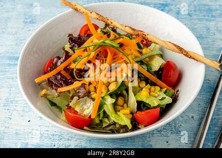 Insalata mista sana in ciotola bianca su tavolo di legno. Insalata mediterranea Foto Stock