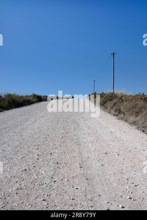 Strada vuota con una linea elettrica e alcuni pali accanto ad essa in una zona rurale del Portogallo Foto Stock