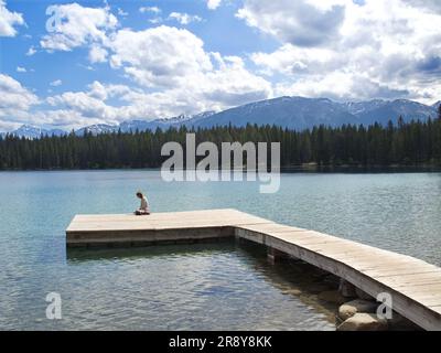Giovane donna sul molo che si affaccia sul lago Maligne nelle Montagne Rocciose canadesi dell'Alberta Foto Stock