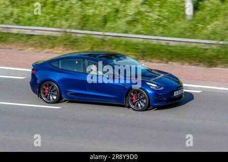 2022 Blue Tesla Model 3 Long Range AWD; viaggia a velocità sostenuta sull'autostrada M6 a Greater Manchester, Regno Unito Foto Stock