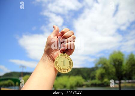 Sfocate di mani femminili sollevate e con medaglie d'oro con nastro tailandese su sfondo blu cielo per mostrare il successo nello sport o negli affari, i vincitori succhiano Foto Stock