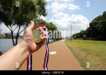 Sfocate di mani femminili sollevate e con medaglie d'oro con nastro tailandese su sfondo blu cielo per mostrare il successo nello sport o negli affari, i vincitori succhiano Foto Stock