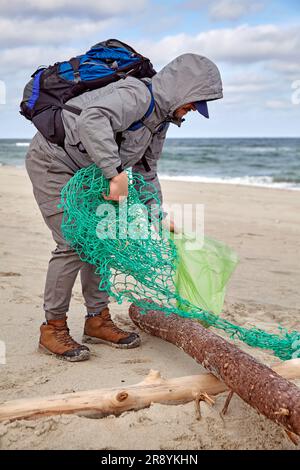 il volontario maschile raccoglie i rifiuti lanciati da una tempesta su una spiaggia sabbiosa con il vento Foto Stock