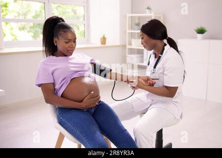 Primo piano del medico di Female misurazione della pressione sanguigna di donna incinta in clinica Foto Stock