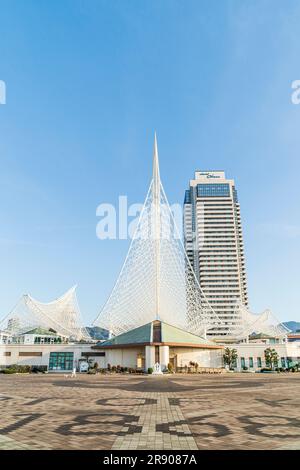 Il famoso Museo marittimo di Kobe con la sua struttura angolata in metallo bianco sopra che ricorda lo scafo di una nave, e l'Okura Hotel contro un cielo azzurro Foto Stock