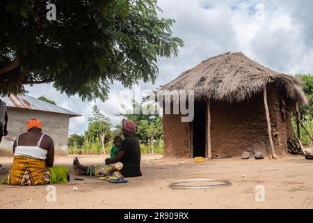 Vecchia signora della tribù Makonde seduta in una cucina primitiva e preparando un pasto tradizionale locale. Semplice vaso metallico in fiamme tra le pietre Foto Stock