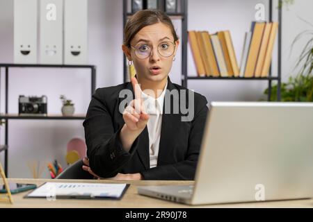 La giovane donna di affari caucasica che lavora sul computer portatile scuote il dito, dicendo No fate attenzione a scossare e dare consigli per evitare pericolo errore disapprovazione segno in ufficio. Fidata ragazza freelance Foto Stock