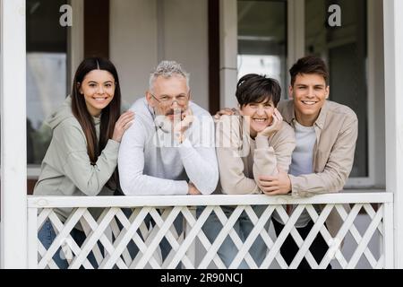 happy parents day, genitori di mezza età sorridenti accanto a una figlia adolescente e un figlio adulto sul portico della casa estiva, riunione di famiglia, legame, momenti Foto Stock